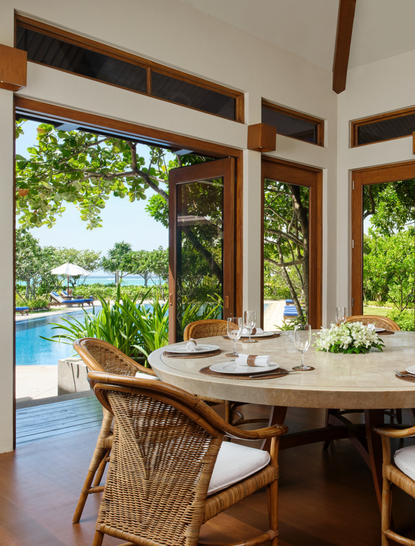 アマンプロのリゾートにあるダイニングルーム。大きな窓からプールと庭園が見え、籐製の椅子が置かれた円形のテーブル。