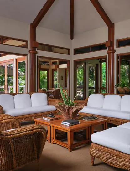 Salle intérieure lumineuse avec sièges en rotin, plantes vertes et baies vitrées donnant sur la nature à Amanpulo resort.