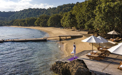 Yoga platform overlooking the beach at Amanwana, Indonesia, with loungers and tropical forest beyond.