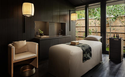 アマン京都のスパトリートメントルーム。大きな窓から庭園を望む落ち着いた空間で、ベッドと読書用の椅子が配置されている。