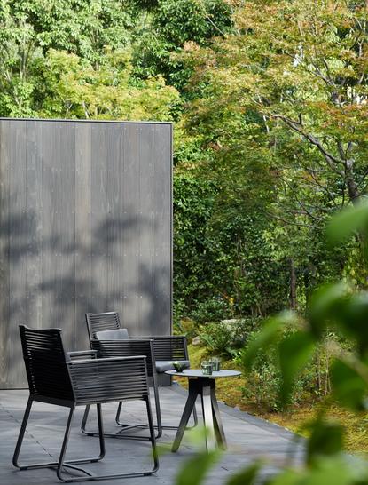 Seating area at Aman Kyoto with black chairs and susuki grass terrace, surrounded by verdant vegetation.