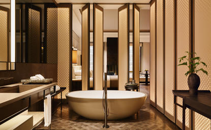 アマン ニューヨークのジュニアスイートバスルーム。ベージュのタイル壁に囲まれた円形バスタブと洗面台。