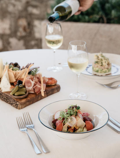 Dining table at Aman Sveti Stefan with fresh salads, cured meats, and wine being poured into glasses.