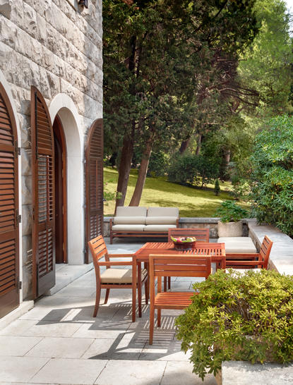 Terrace at Aman Sveti Stefan with wooden dining table, chairs, and views towards tree-lined grounds.