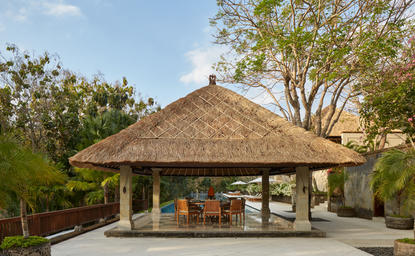 Dining bale with thatched roof at Aman Villas at Nusa Dua, Indonesia, surrounded by tropical greenery.
