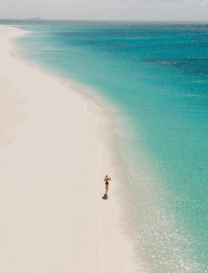 Solo figure walking along a pristine white sand beach with turquoise waters at Amanpulo, Philippines.