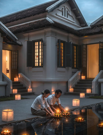 Candlelit courtyard at Amantaka during Loy Krathong celebration, with traditional wooden architecture and warm lantern glow at dusk.