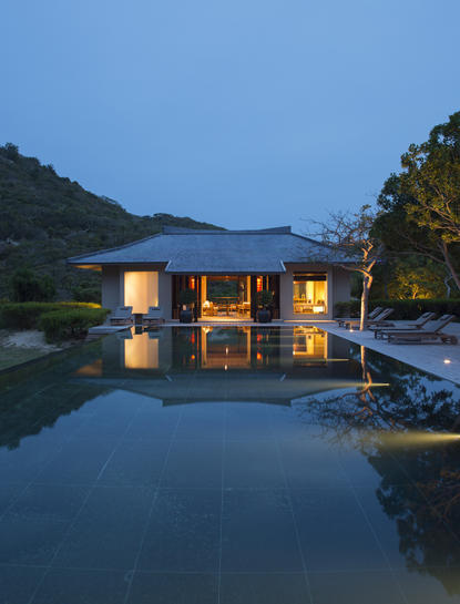 安缦诺怡度假村内，灯火通明的现代建筑倒映在宁静的池水中，夜幕降临。