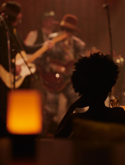 Silhouetted figure watching a jazz performance at Aman New York's The Tangiers club, with musicians on stage bathed in warm amber light.