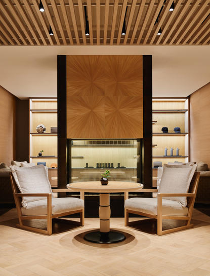 Area relax della spa presso Aman New York, con poltroncine in pelle, camino centrale e soffitto in legno.