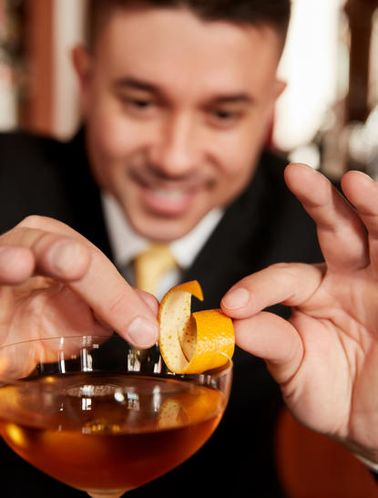 Antonio, Aman Venice staff member, holds a cocktail garnished with citrus peel.