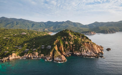 安缦诺怡度假村沿岸，金色岩石山峰从翠绿海水中升起，背景为雾笼群山。