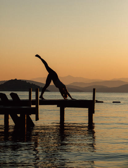 Silhouetted figure practising yoga on a wooden jetty at Amanruya at sunrise, overlooking calm waters.