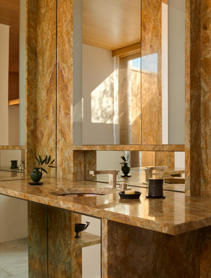 Marble bathroom vanity with wooden mirror frame at Amanzoe, featuring natural light and toiletries.