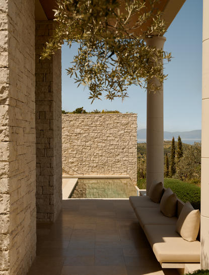 Covered pavilion with stone columns overlooking the pool at Amanzoe, with cypress trees visible beyond.