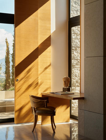 Sunlit pool pavilion at Amanzoe with wooden chair and cypress tree view.