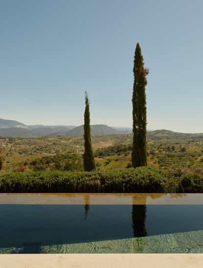 Pool pavilion at Amanzoe with cypress trees and distant mountains reflected in water.