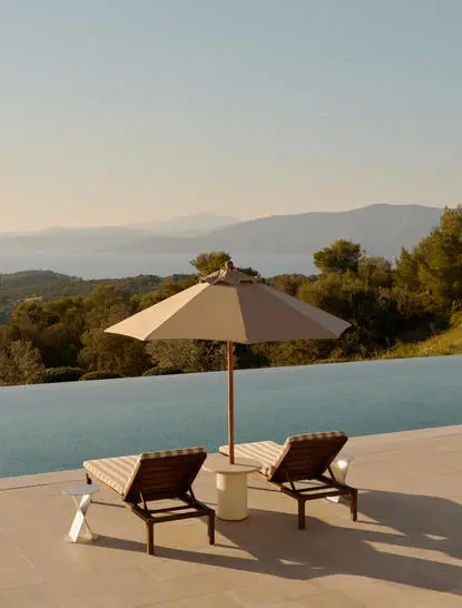 Two sun loungers and umbrella on a terrace overlooking mountains at Amanzoe.
