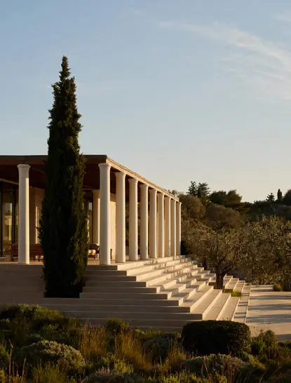 Villa at Amanzoe with columned façade and cypress tree at sunrise.