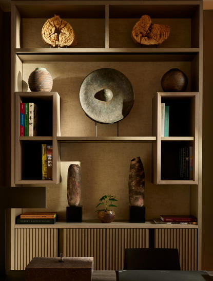 Espace bureau de la suite Aman à Aman New York, avec étagères en bois affichant objets décoratifs et livres.