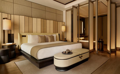 アマン ニューヨークのジュニアスイートの寝室。ベージュと木調の温かみのある内装で、キングサイズベッドとモダンなベンチシートが配置されている。