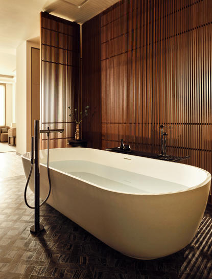 Salle de bains d'une suite trois chambres à Aman New York, avec baignoire autoportante blanche et panneaux de bois sombre.
