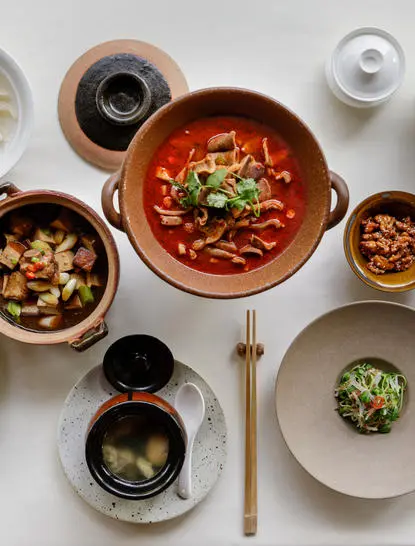 Overhead view of Amanyangyun dining with bowls of traditional Chinese dishes and condiments arranged on white surface.