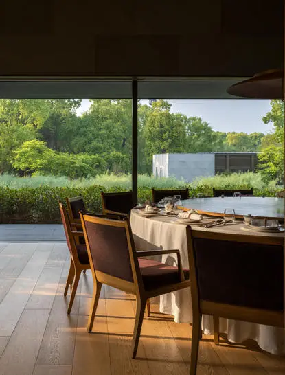 Dining area at Amanyangyun with wooden chairs at table, overlooking verdant garden through large windows.