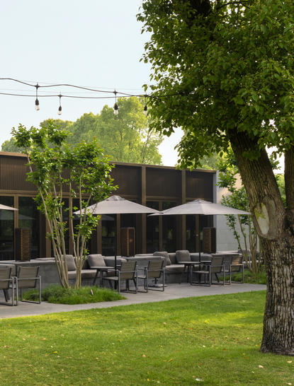 Outdoor seating area at Amanyangyun's China restaurant Yinlu, with dining tables beneath umbrellas and mature trees.