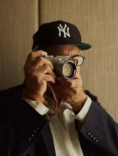Homem usando boné Yankees e óculos, segurando câmera fotográfica na Aman New York.