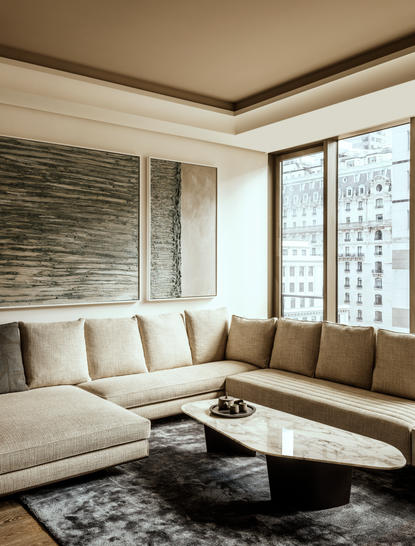 Living room at Aman New York with L-shaped seating, textured accent wall, and floor-to-ceiling windows overlooking the city.