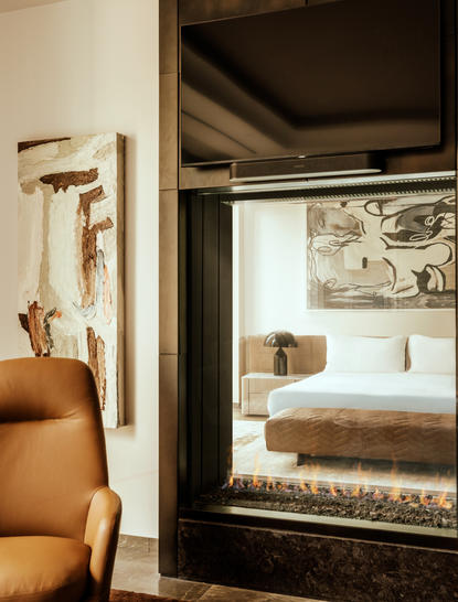 Bedroom at Aman New York seen through an open doorway, with warm wood tones and natural light filtering through.