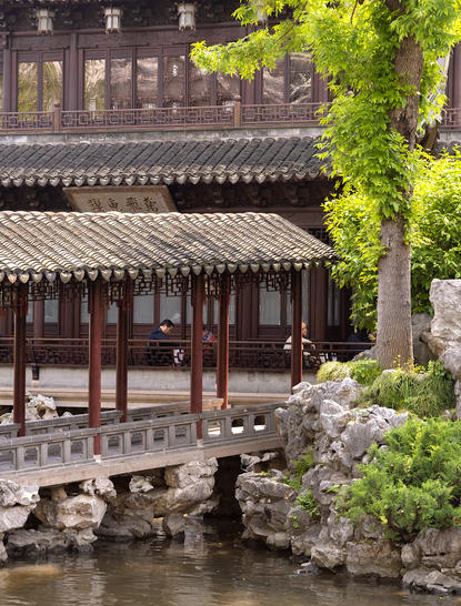 Amanyangyun courtyard with traditional architecture, ornamental bridge and lush greenery reflected in still water.