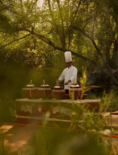 A chef prepares a meal at a wooden table set amongst jungle foliage at Aman-i-Khas.