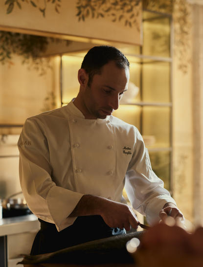 Chef in the kitchen at Aman Venice, preparing a dish with focused attention.