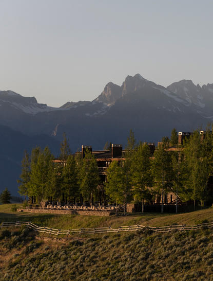 Amangani exterior in spring with forested grounds and mountain backdrop, Jackson Hole.