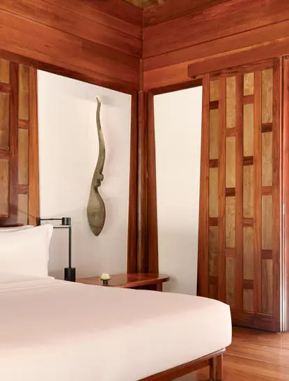 Pavilion bedroom with warm timber walls and a white bed at Amanpuri resort.