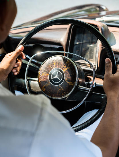 Guest's hands on steering wheel of vintage car at Amansara, Cambodia.