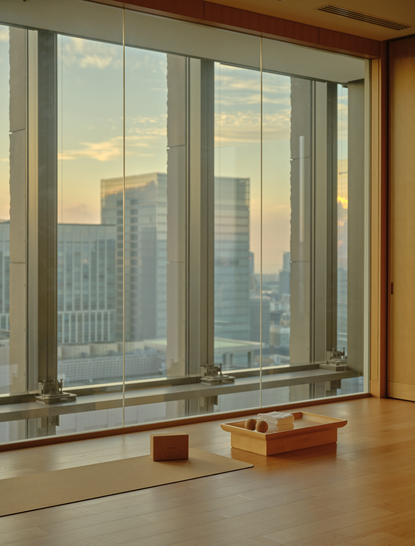 Spa and wellness yoga room at Aman Tokyo with floor-to-ceiling windows overlooking the city skyline at golden hour.