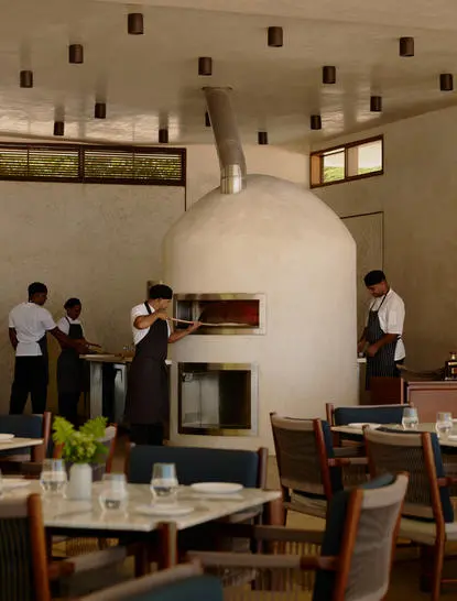 Four diners gathered around wooden tables near a traditional pizza oven at Amanera resort's beach club.