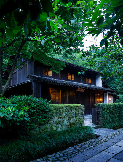 A traditional Chinese pavilion nestled amongst lush greenery at Amanfayun, illuminated warmly as dusk falls.
