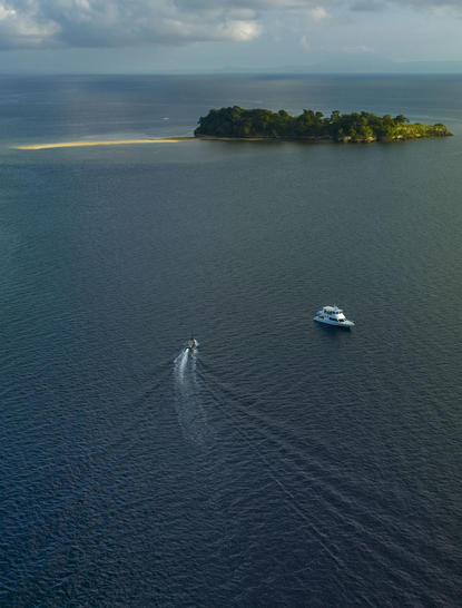 Aerial view of a speedboat approaching a small forested island in Saleh Bay, Sumbawa, Indonesia, where Amanwana is located.