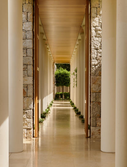 安缦卓熠度假村的走廊，两侧装饰石墙，尽头可见绿色植物。