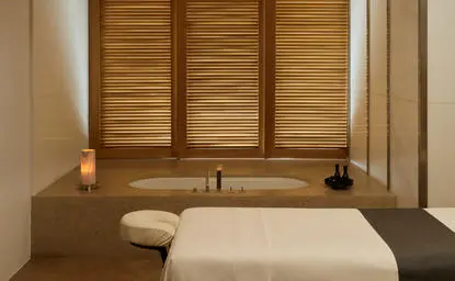 Spa treatment room at Amanzoe resort with wooden shutters, neutral tones, and a massage table.