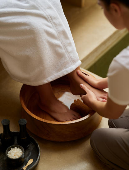 Therapist's hands guiding a guest's foot into a warm water bowl during a spa treatment at Amanzoe resort.