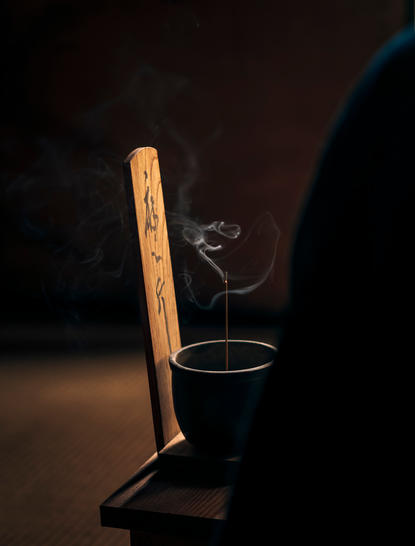 Incense stick burning in holder at Aman Kyoto resort, smoke curling gently against dark background.