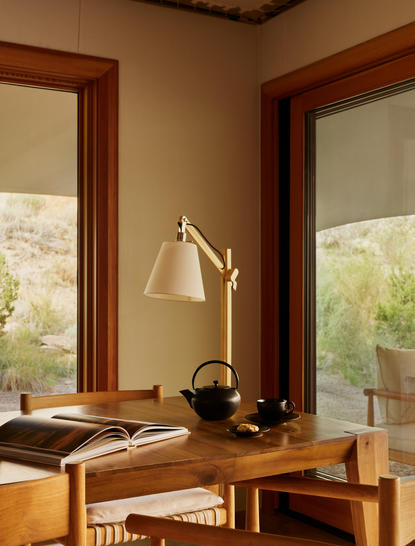 Camp Sarika accommodation pavilion at Amangiri with wooden desk, brass lamp and desert views through large windows.