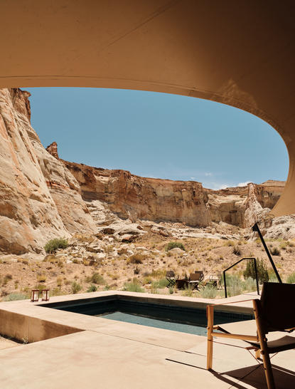 Wooden bench facing plunge pool at Amangiri pavilion, framed by canyon rock formations under clear sky.
