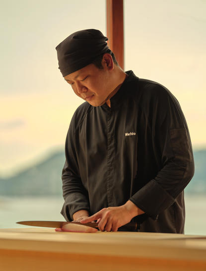 Man in dark jacket at Amanpuri overlooking coastal landscape at sunset.