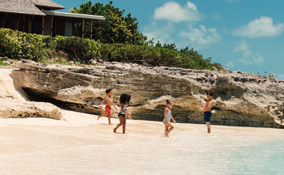 Children playing on a sandy beach beside a large driftwood log at Amanyara's dedicated kids club.